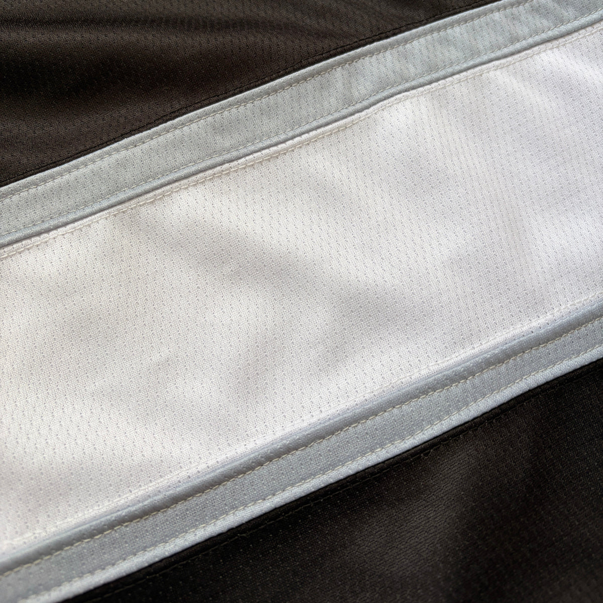 Close-up of a white athletic mesh fabric panel bordered by light gray trim, set against a dark brown background.