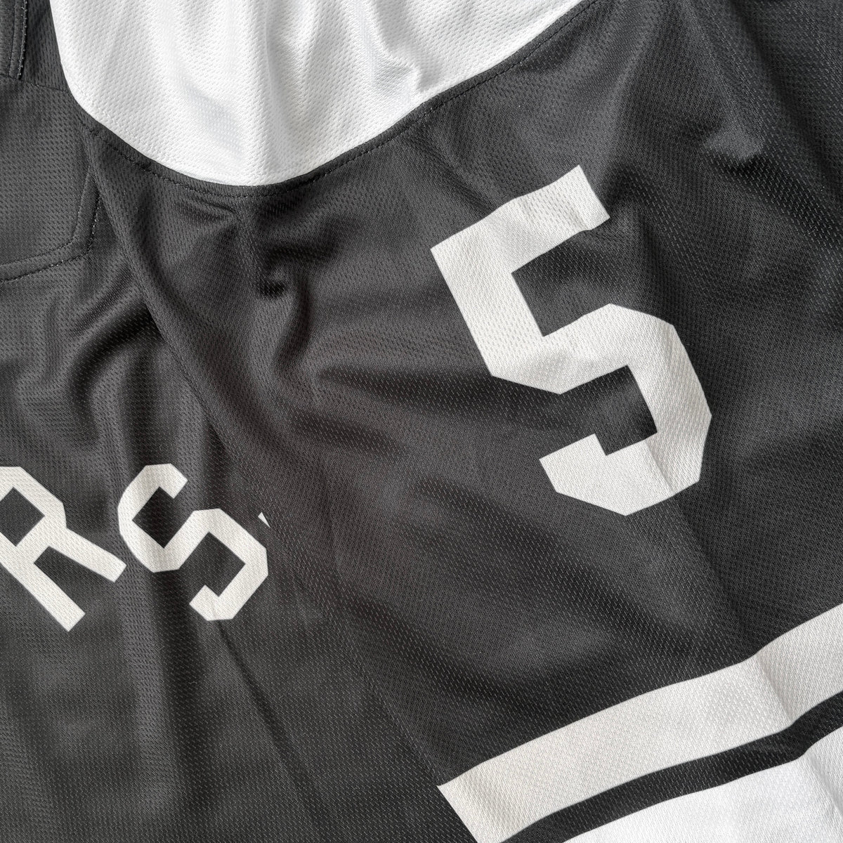 Close-up of a black and white athletic jersey with large white lettering and the number 5, laid flat.