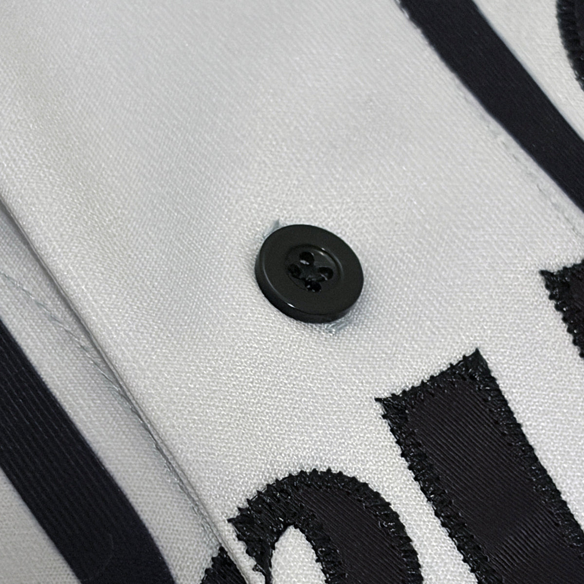 Close-up of a white fabric garment with black embroidered lettering and black buttons.
