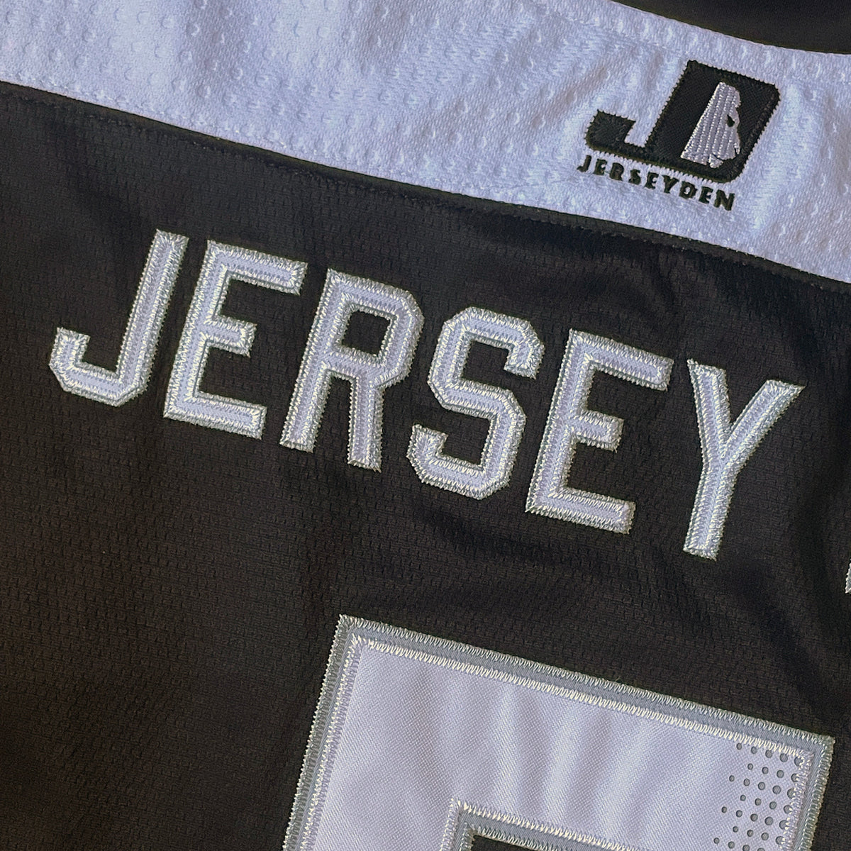 Close-up of a black and white JERSEY jersey showing the JERSEY text, a large white number 5, and the JERSEYDEN brand logo on the shoulder.