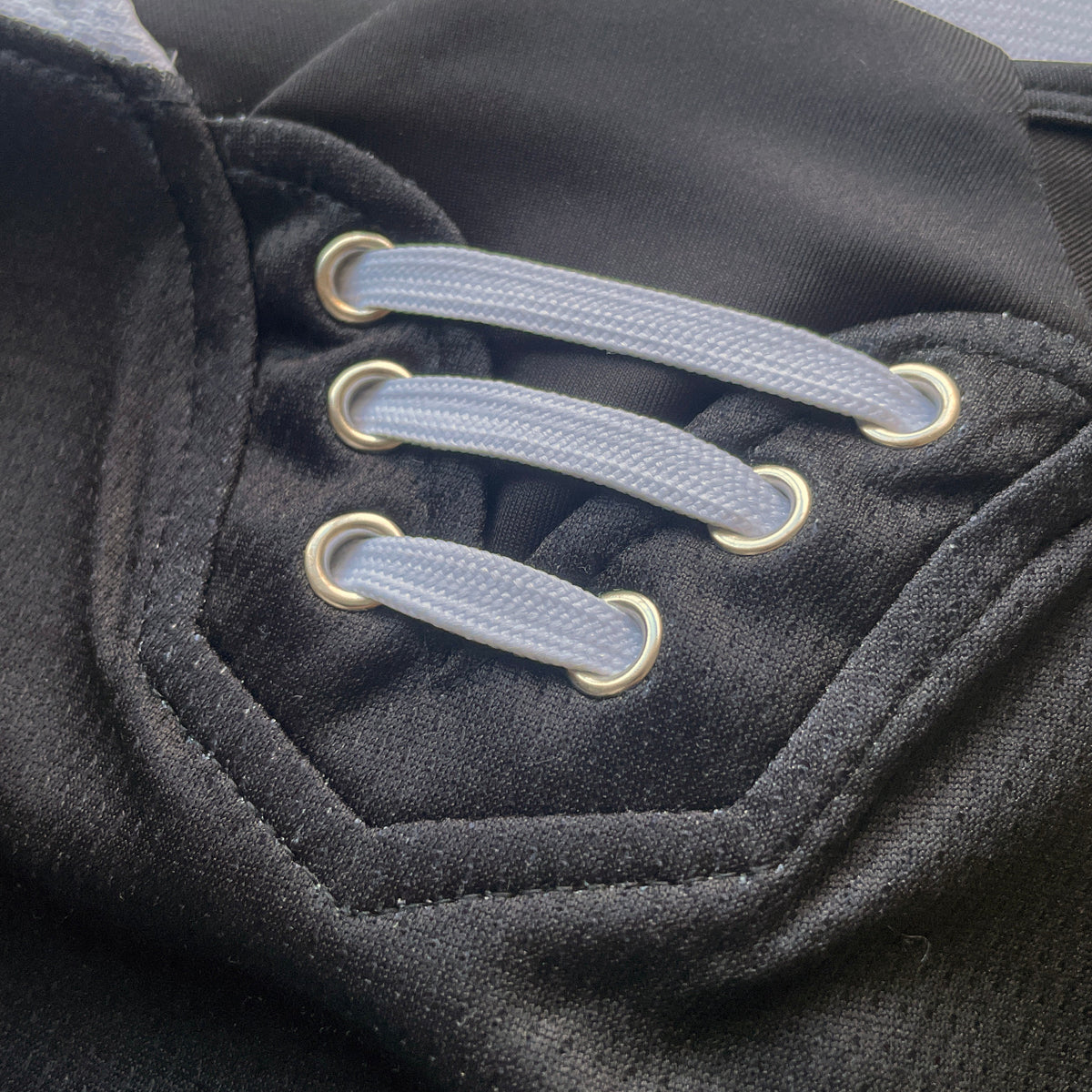 Close-up of a black lace-up item with light gray laces threaded through gold metal eyelets.