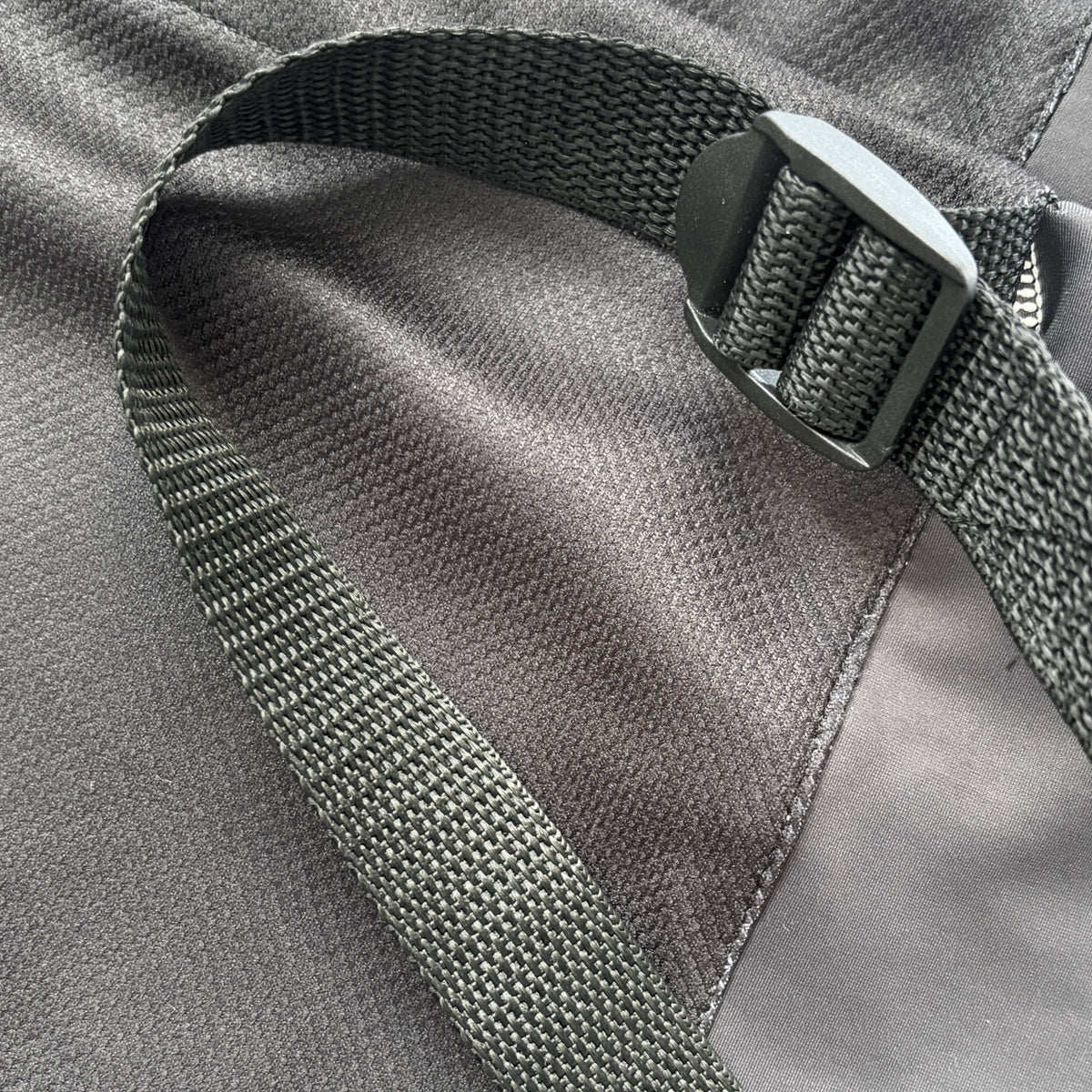 Close-up of a gray adjustable drawstring with a metal slider, attached to a gray fabric garment, with a light blue quilted blanket in the background.