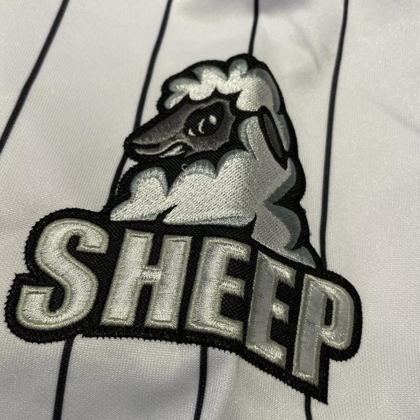 A close-up of a white pinstriped fabric with a large embroidered patch featuring a sheep head above the word "SHEEP" in bold letters.