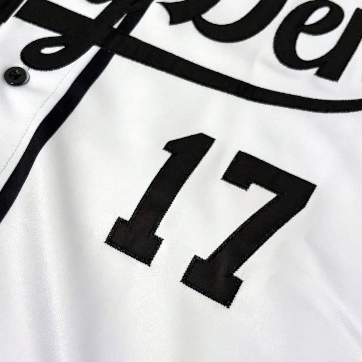 Close-up of a white baseball jersey with black embroidered lettering and the number 17.