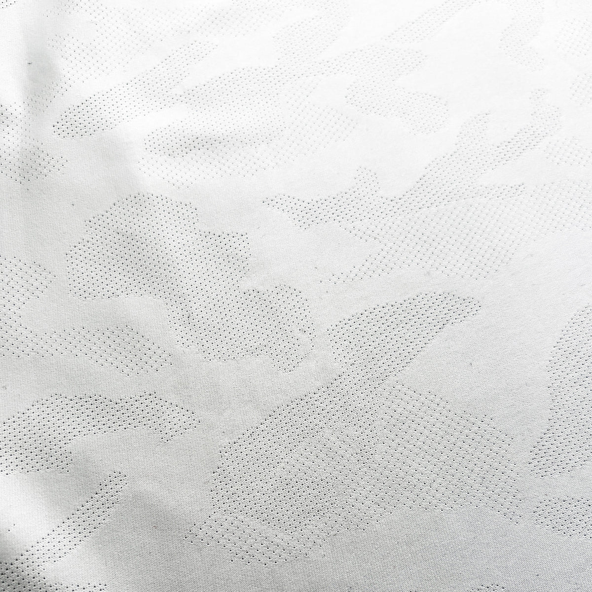 A close-up of a white textured fabric with a subtle, tonal camouflage pattern made of small stitched dots.