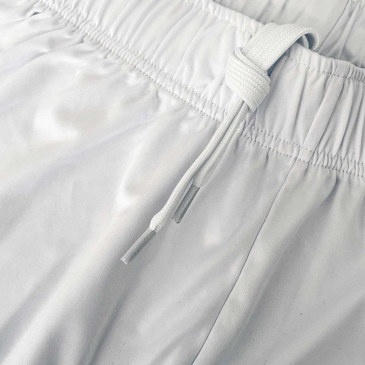 Close-up of white athletic shorts showing the elastic waistband and drawstring.