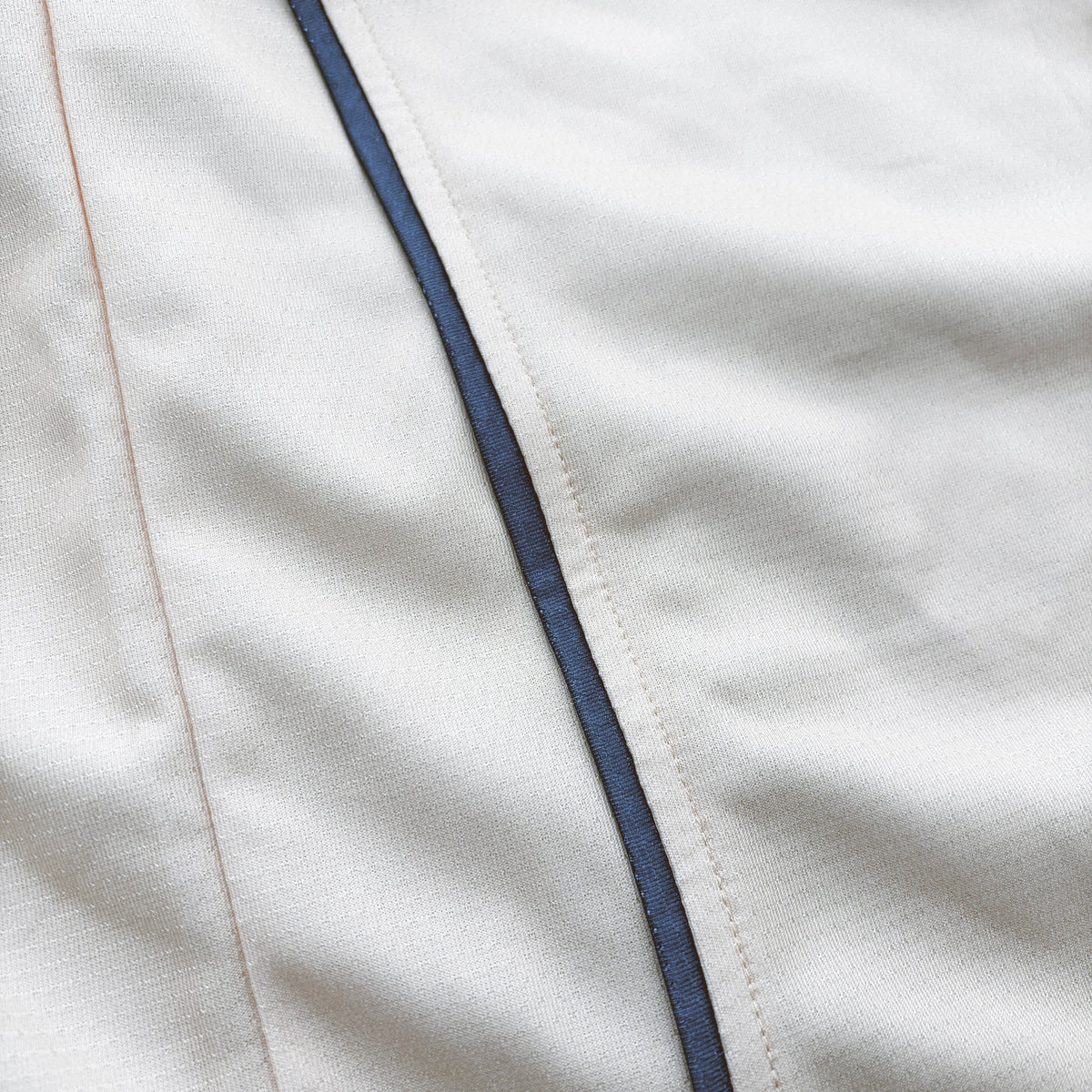 Close-up of a white fabric surface with a thin dark navy piping detail running vertically.