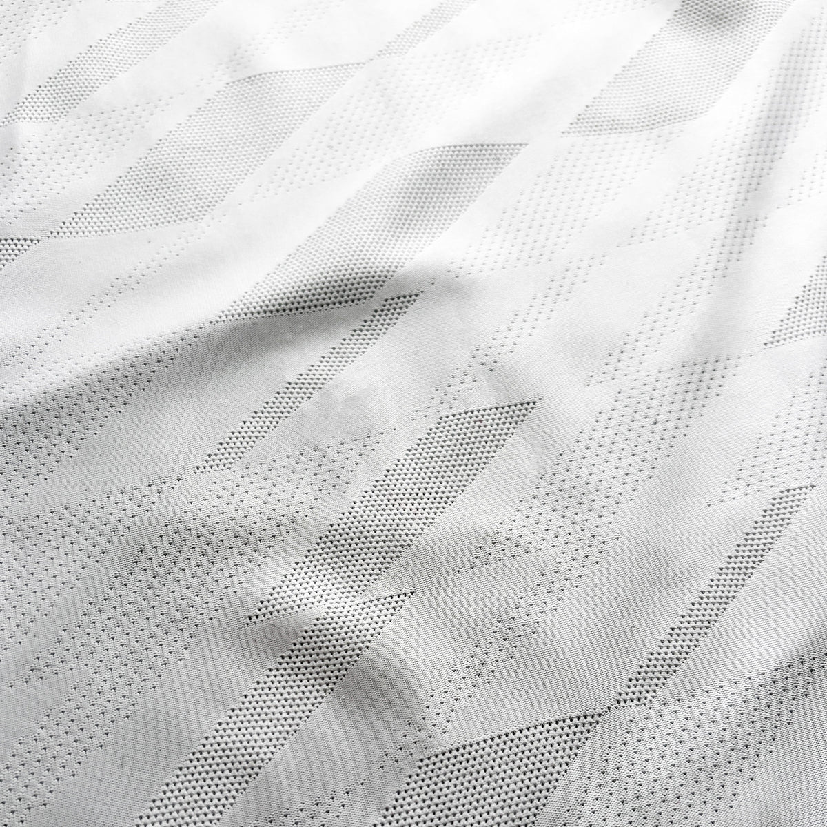 A close-up of a white textured fabric with a geometric pattern of small perforated dots forming diagonal stripes.