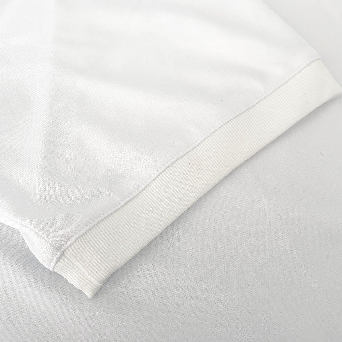 Close-up of a white athletic jersey sleeve with a ribbed cuff, laid flat on a light surface.